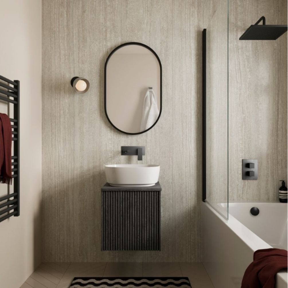 Lifestyle image of the Showerwall Laminate Romano Travertine 2440mm x 579mm Proclick MDF Wall Panel - SW86 installed on a bathroom wall behind a small wall-hung vanity unit with basin, straight edged bathtub, and oval mirror.